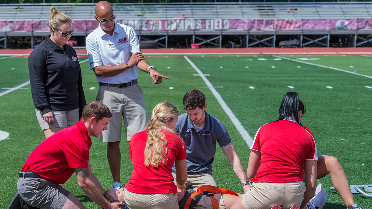Students practicing taking care of an injured player at the Pitt Center and at the football field