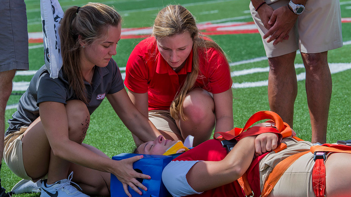 Students practicing taking care of an injured player at the Pitt Center and at the football field