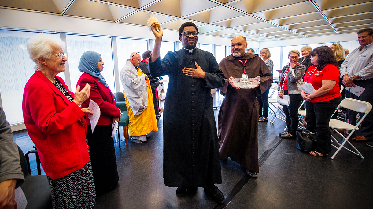 A priest blesses an interfaith prayer space with holy water