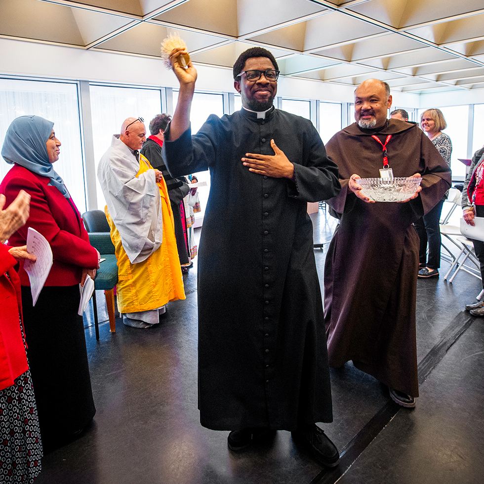 A priest blesses an interfaith prayer space with holy water