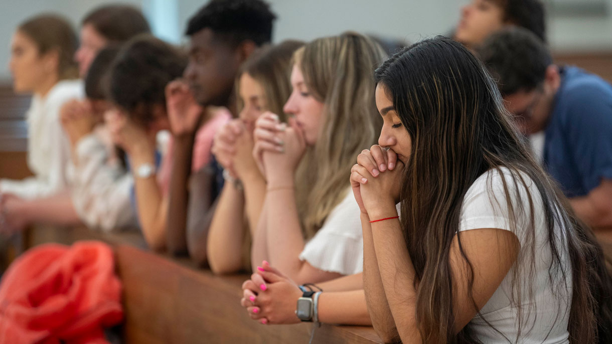 Students kneeling in the pews and praying with their eyes closed