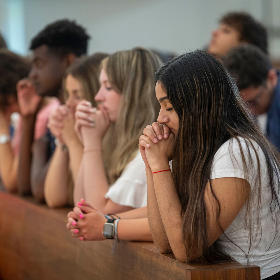 Students kneeling in the pews and praying with their eyes closed