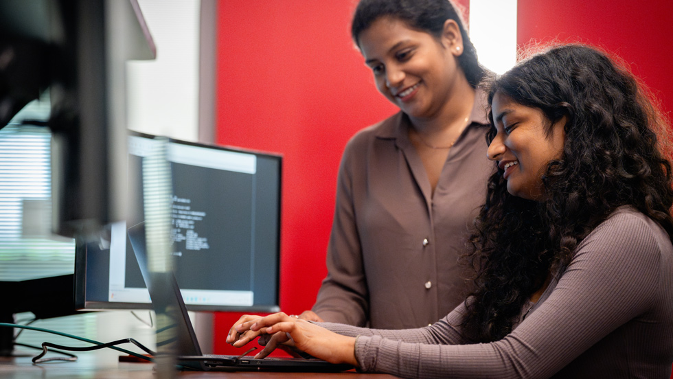 Student working on laptop with professor looking over her shoulder