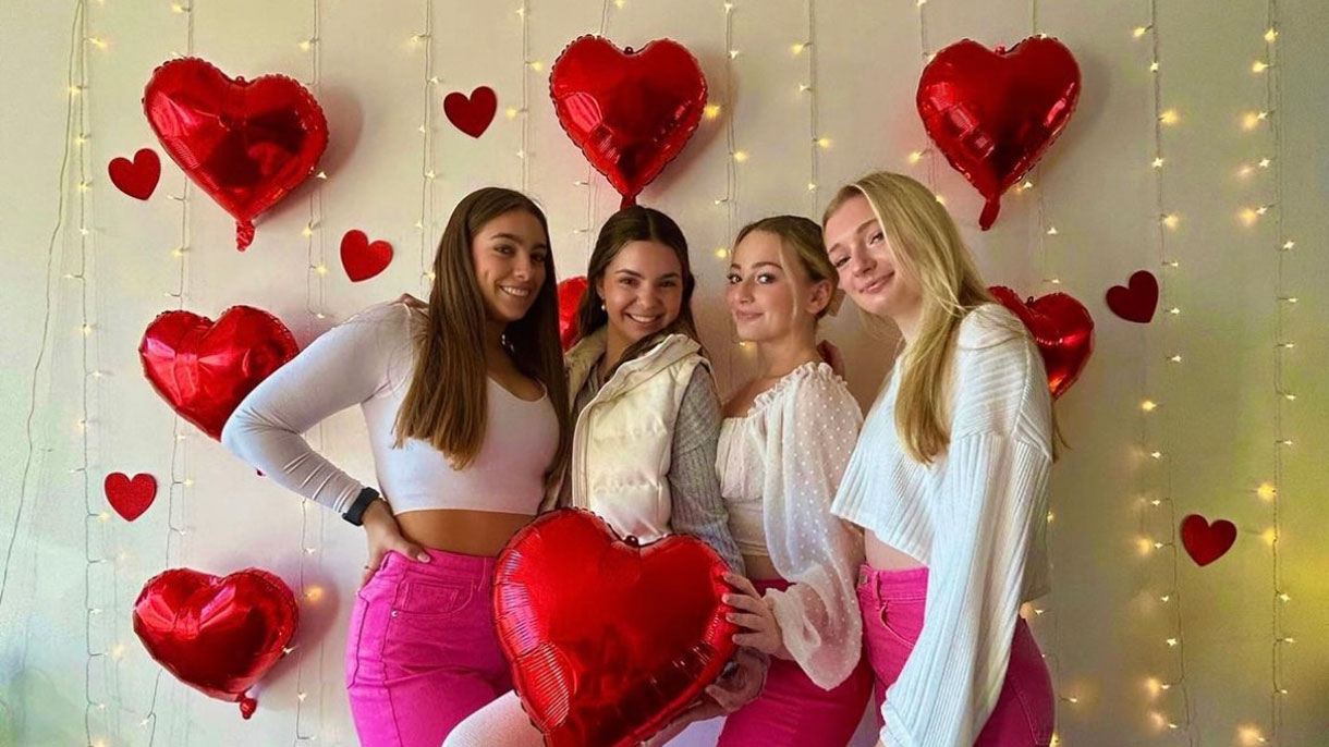 Members of Alpha Delta Pi posing for a photo with heart balloons and twinkling hanging lights in the background