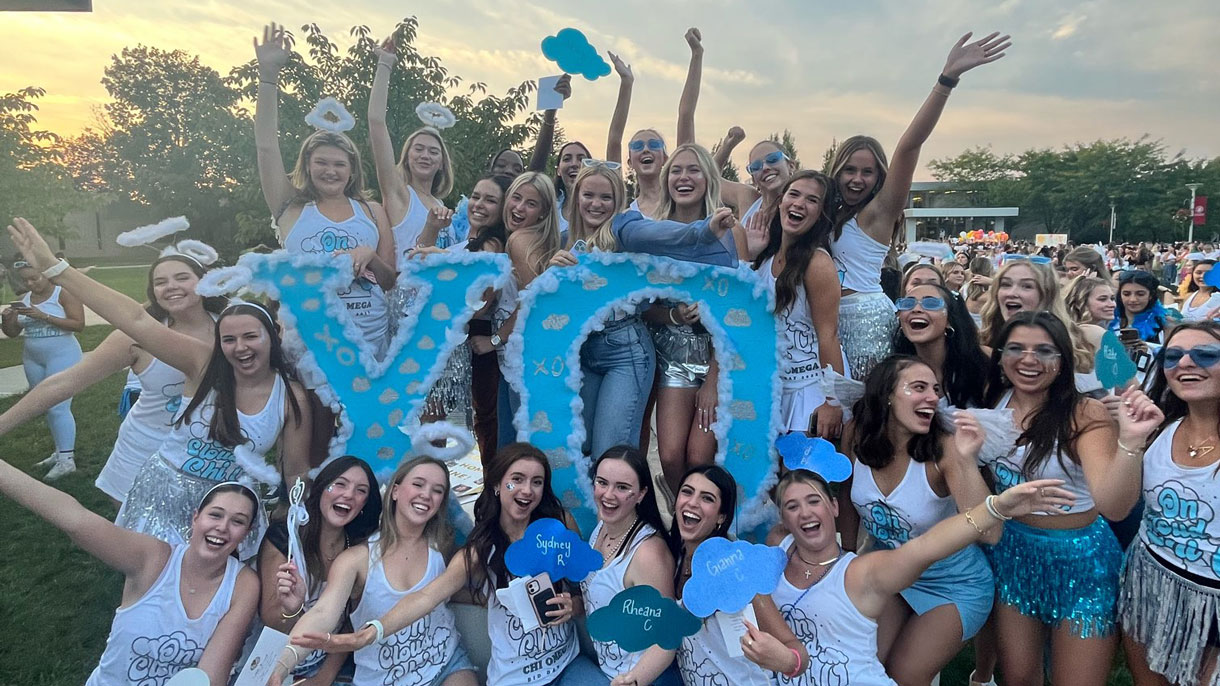 Chi Omega members on bid day smiling with their letters, wearing blue and white