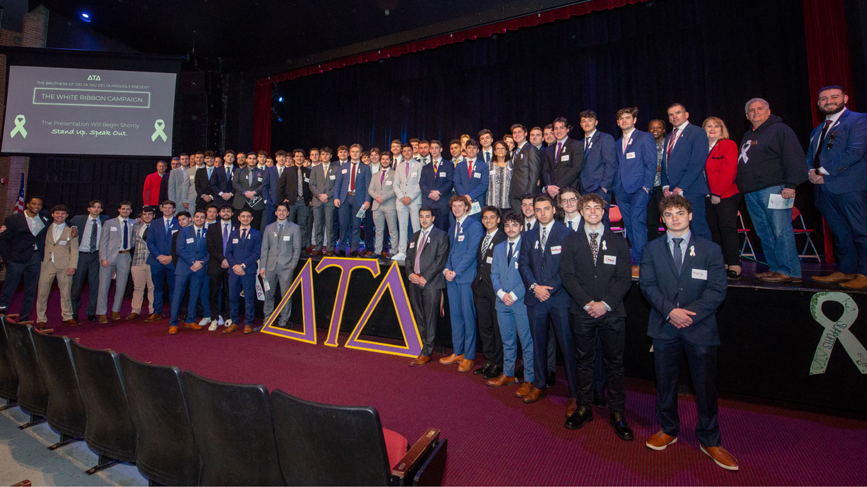 Members of Delta Tau Delta at their philanthropy event. They are all wearing suits and standing in an theater
