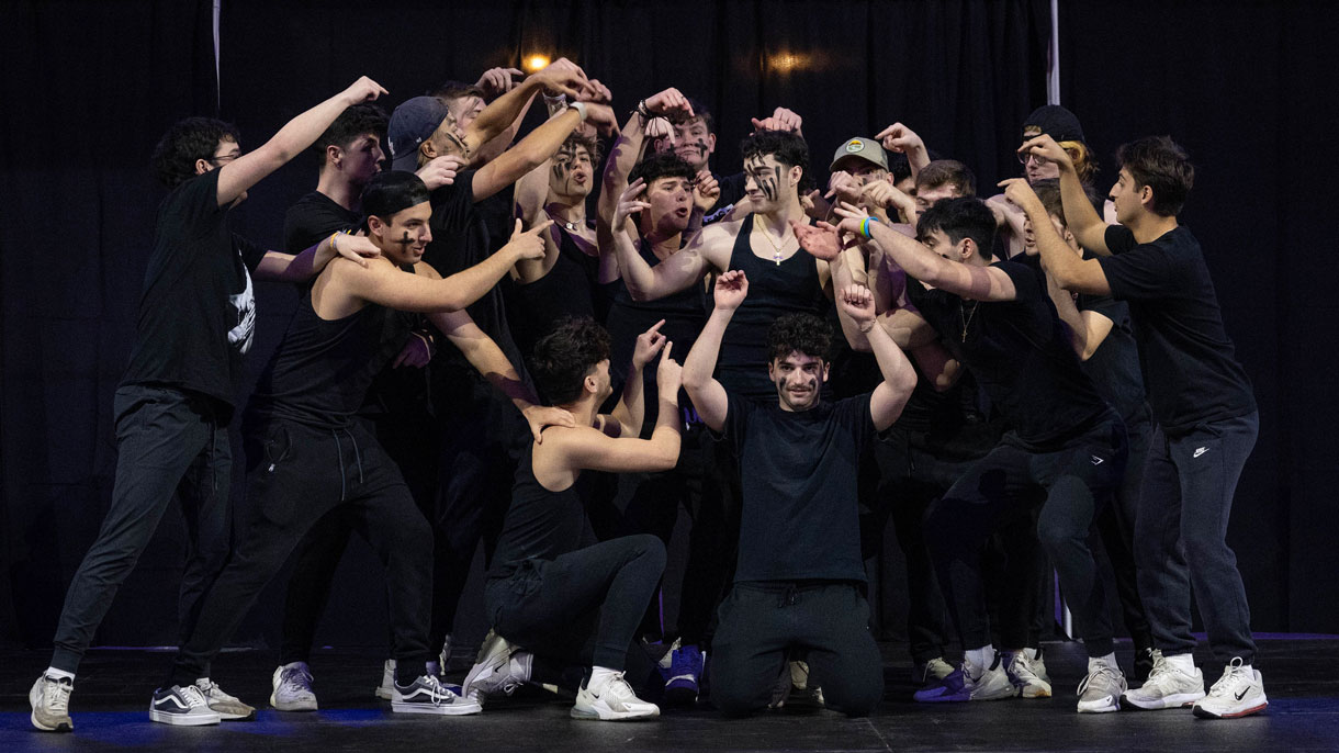 Members of Delta Tau Delta performing in Greek sing. All pointing towards one person and have black painted lines on their faces.
