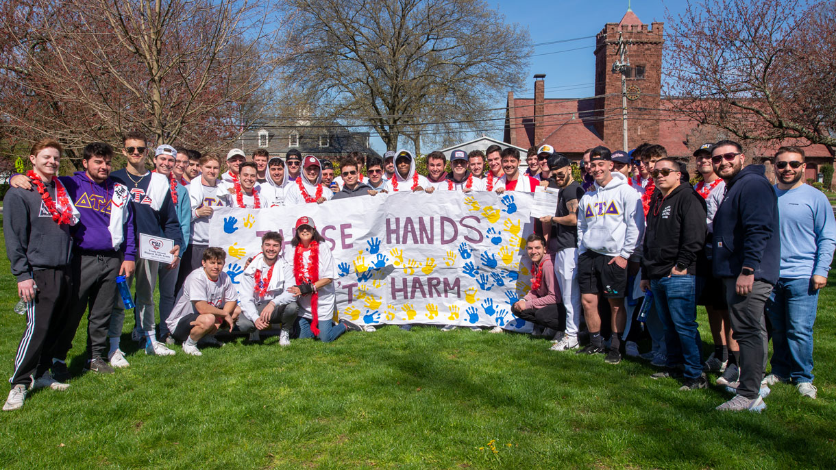 Members of Delta Tau Delta holding a large sign with colorful handprints on it