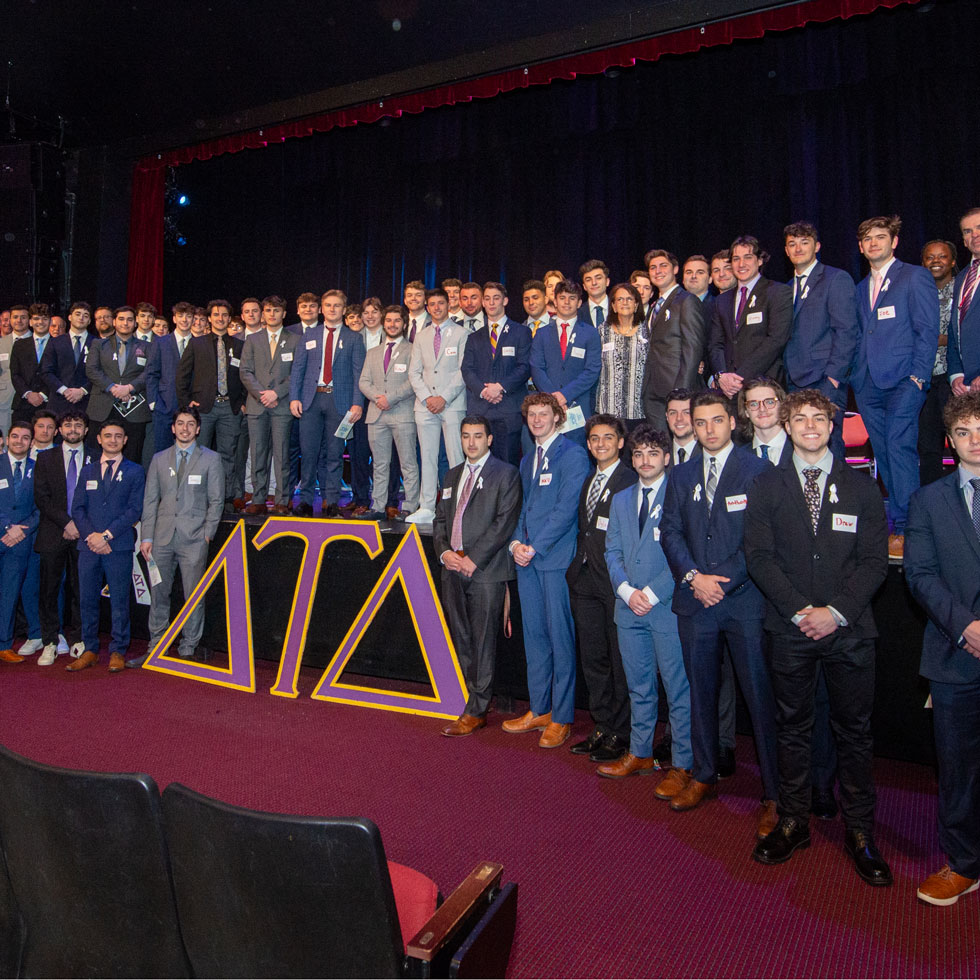 Members of Delta Tau Delta at their philanthropy event. They are all wearing suits and standing in an theater