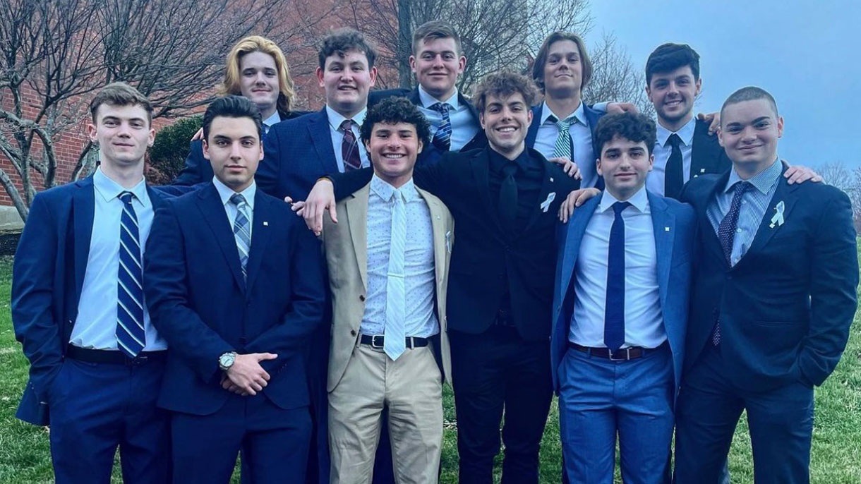 Members of Delta Tau Delta standing behind a rock with their fraternity letters painted on it.
