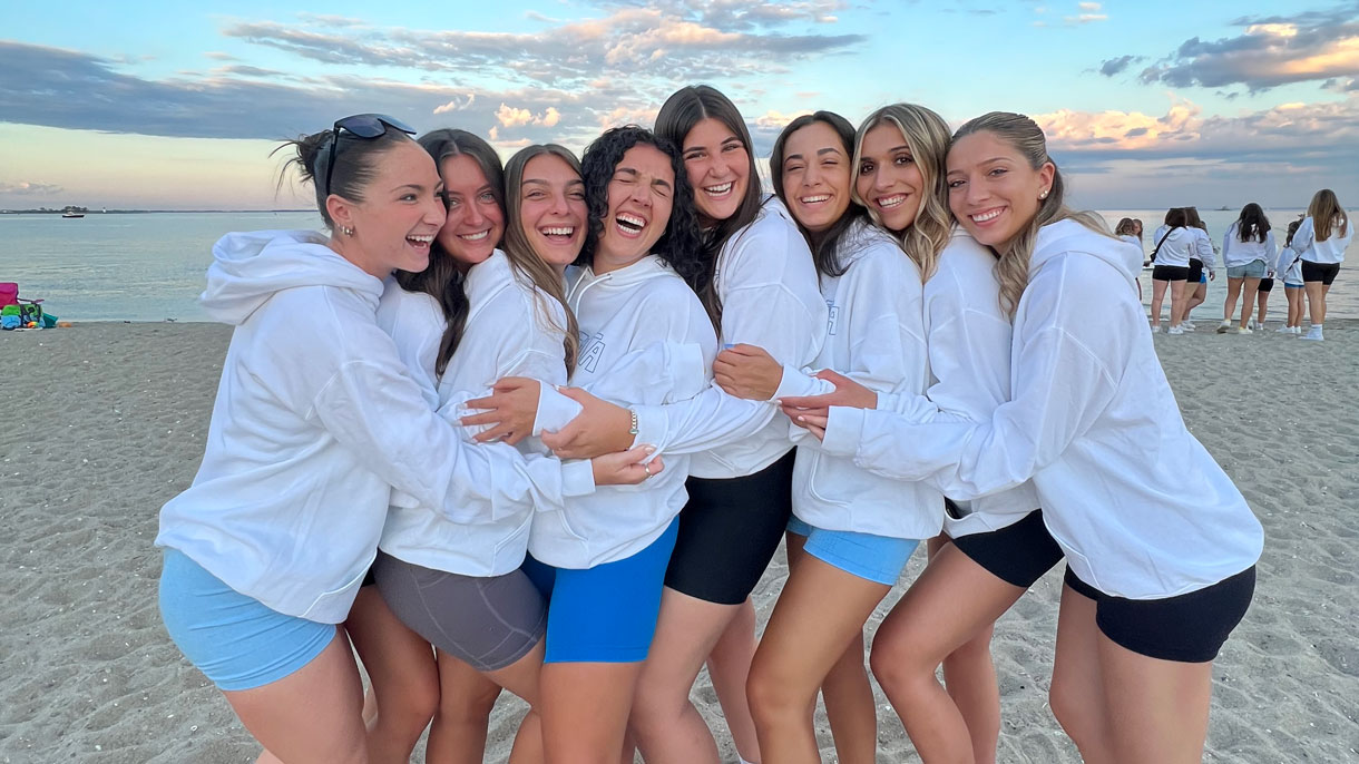 Members of Delta Zeta hugging on a beach, sun setting in the background
