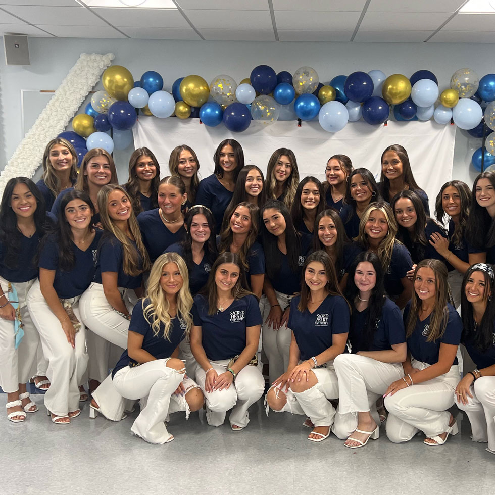 Members of Kappa Delta during recruitment, wearing blue shirt and white pants. Blue and gold balloons in the background