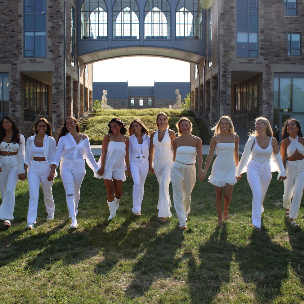 Members of Phi Sigma Sigma wearing white and walking hand in hand
