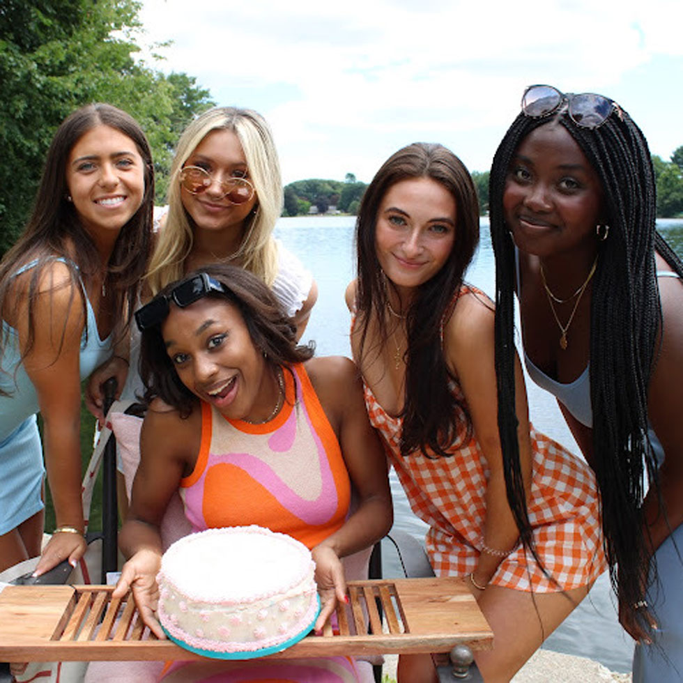 Members of Phi Sigma Sigma posing with a cake. A lake in background