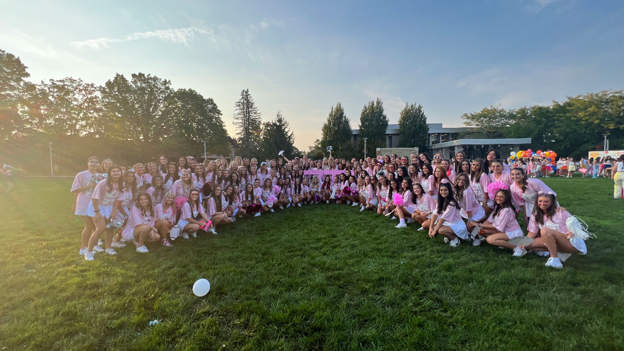 Members of Zeta Tau Alpha at Bid Day wearing pink and white and the sun is setting in the background