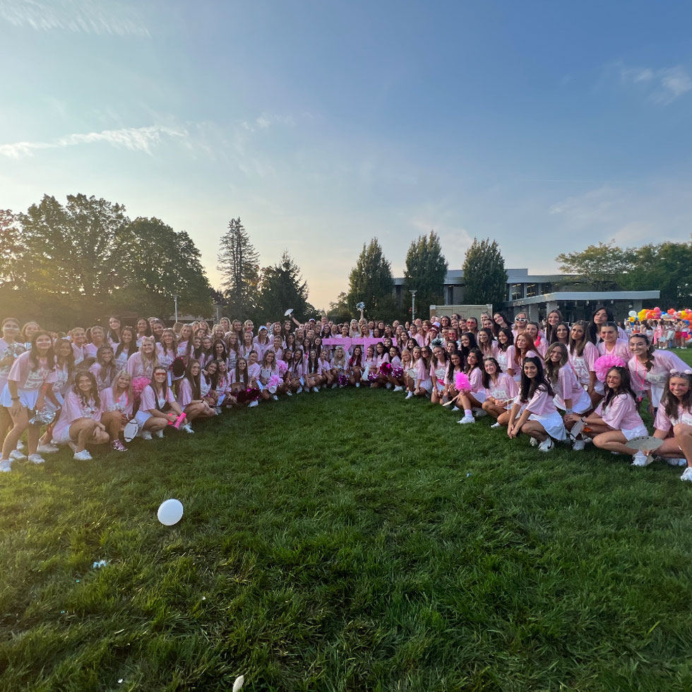 Members of Zeta Tau Alpha at Bid Day wearing pink and white and the sun is setting in the background