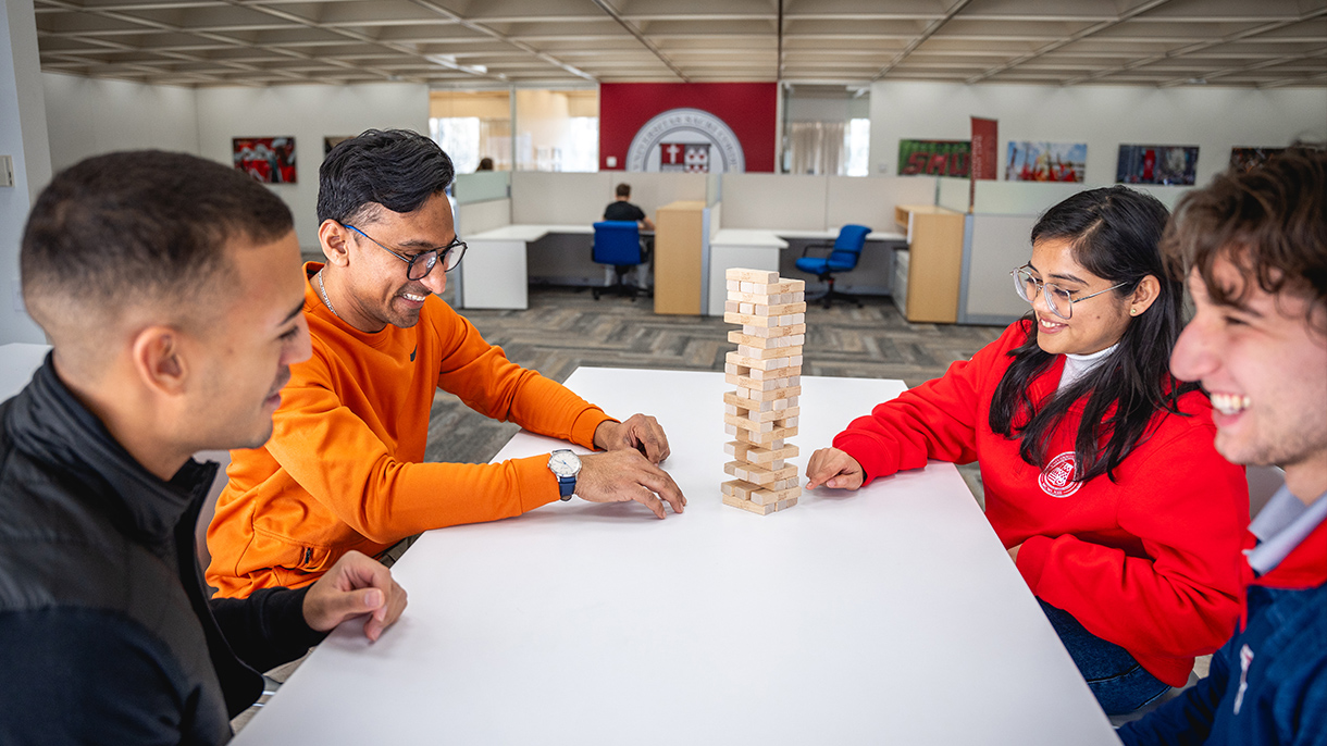 Four people playing the game Jenga in a student lounge