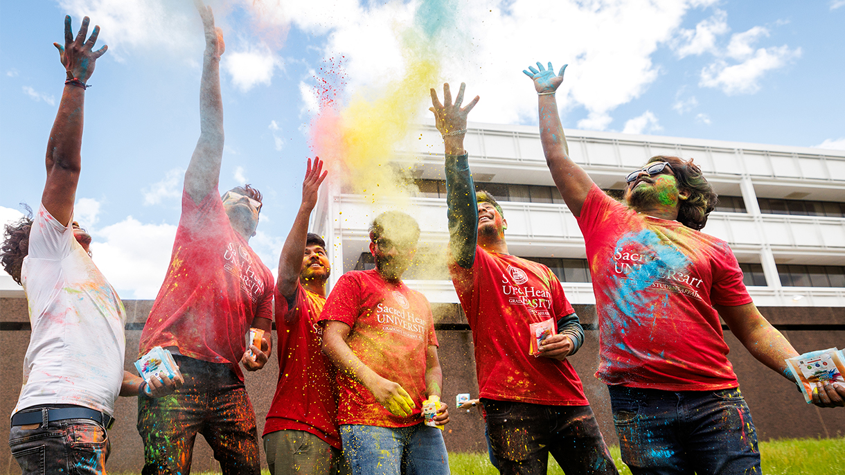 Six people throw colored Holi powders into the air