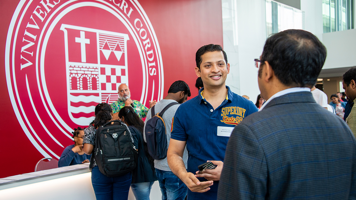 A person smiling and chatting with a faculty member at a college open house event