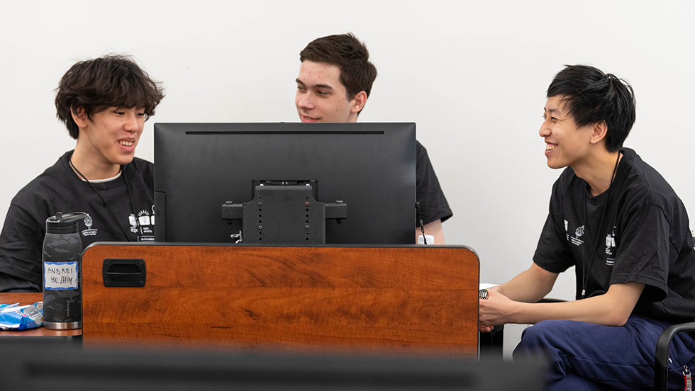 three college students around a desktop computer