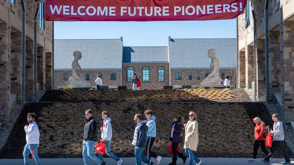 A college tour walking in front of a banner that reads Welcome Future Pioneers