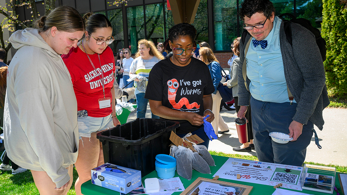 A group of people learning about worm composting at an Earth Day fair