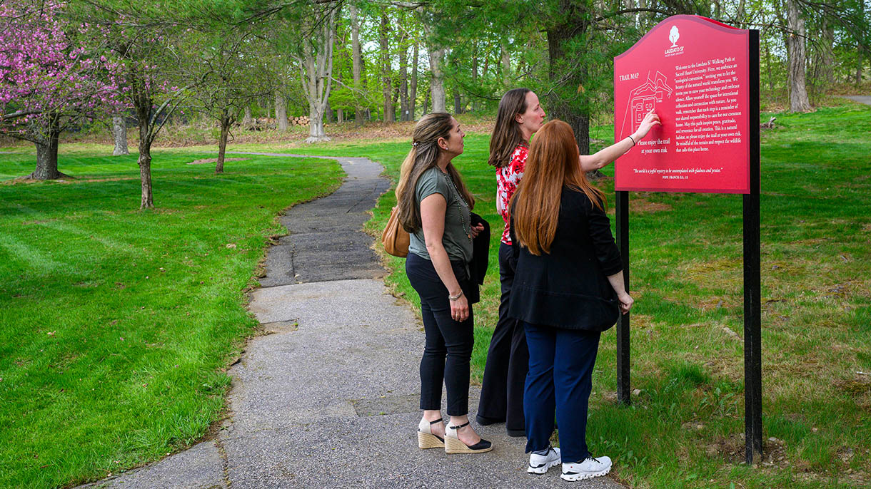 people looking at the Laudato Si walking trail sign at Sacred Heart University