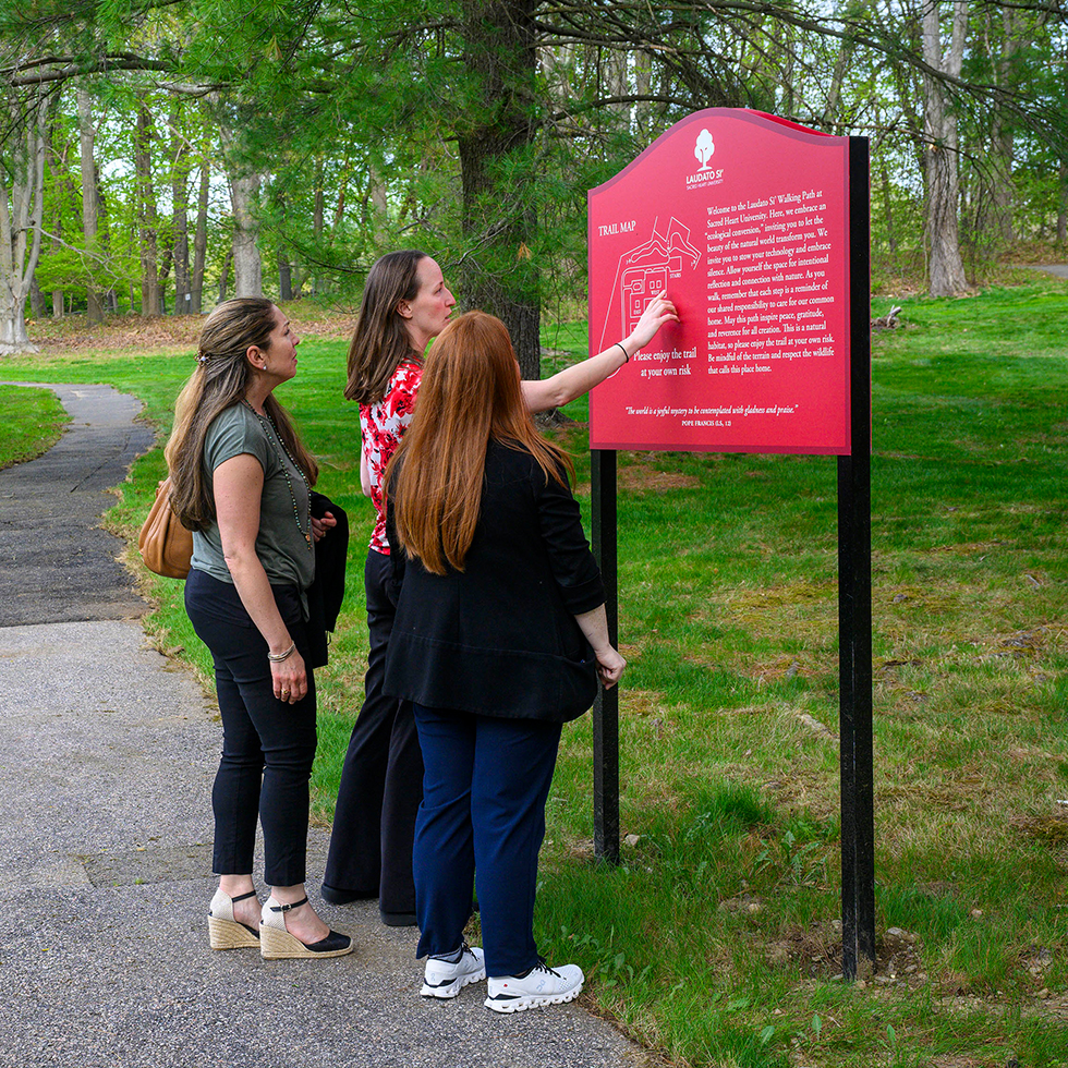 people looking at the Laudato Si walking trail sign at Sacred Heart University