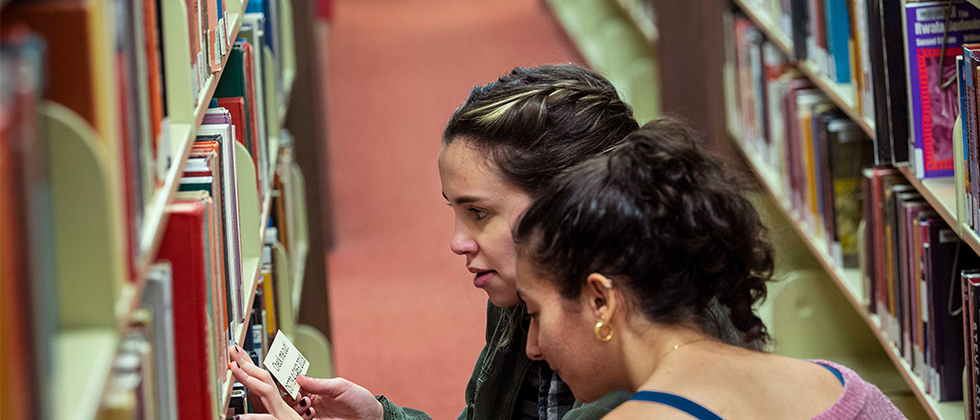 Students looking at books on a shelf in the library