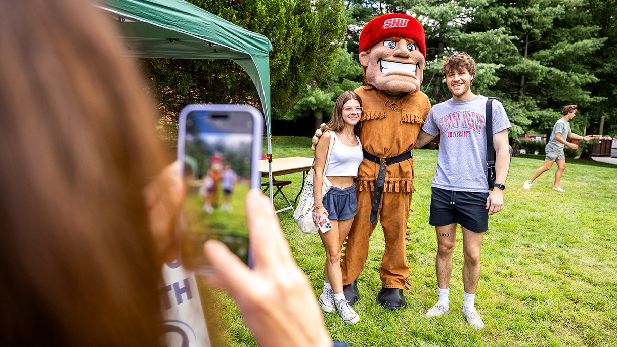 Big Red mascot poses for a photo with two people at a Sacred Heart University open house