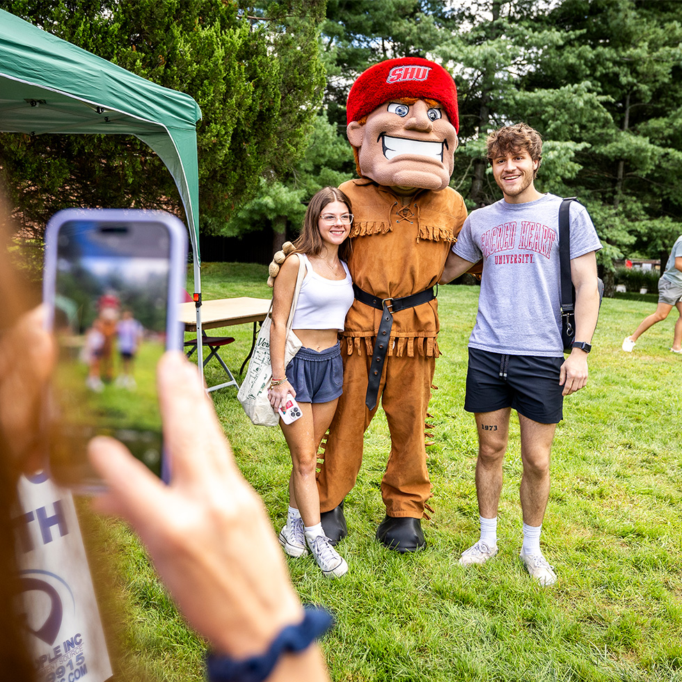 Big Red mascot poses for a photo with two people at a Sacred Heart University open house
