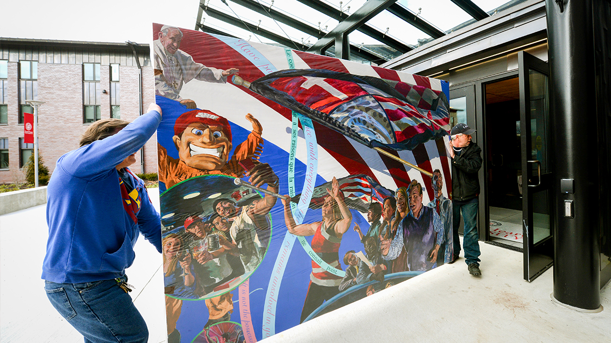 two people carry a mural painting featuring Pope Francis