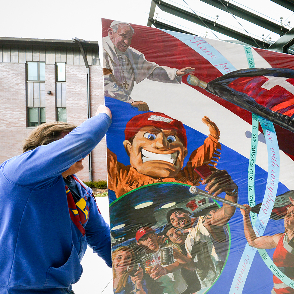 two people carry a mural painting featuring Pope Francis