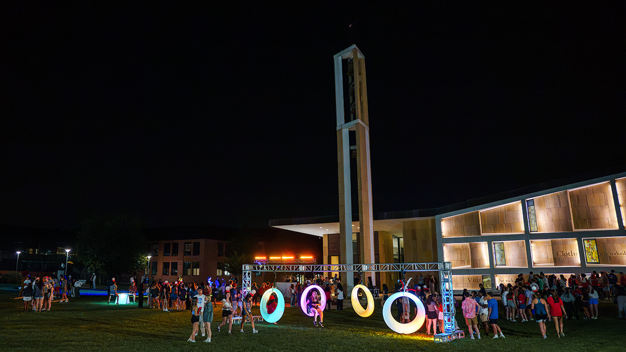 people gathered on a quad at night with light-up swings and a chapel in the background