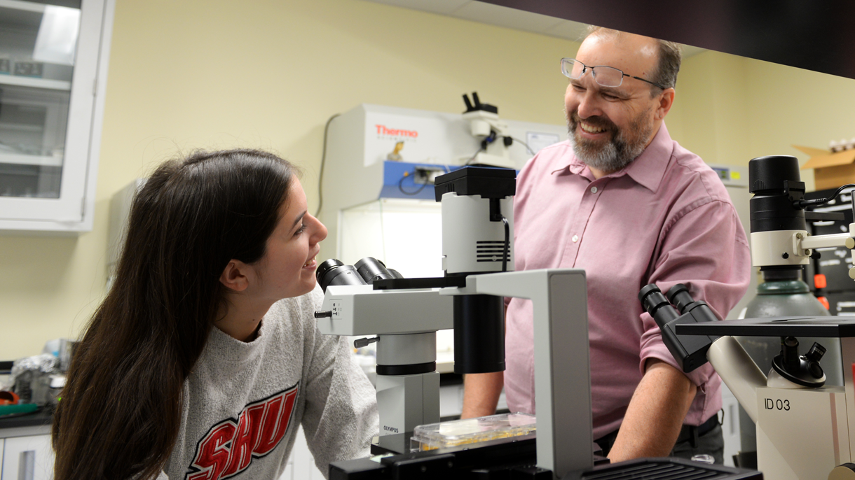 Student and teacher talking over microscope