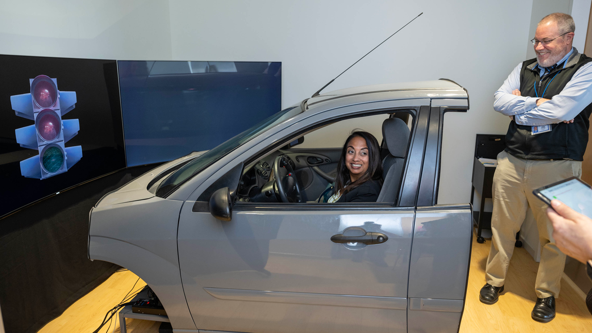 Woman in driving simulator with man looking on