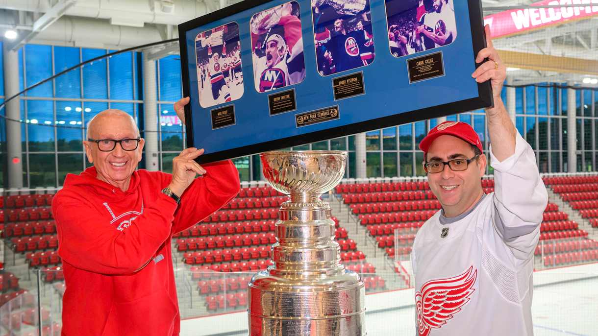 Two men holding framed photos over the Stanley Cup