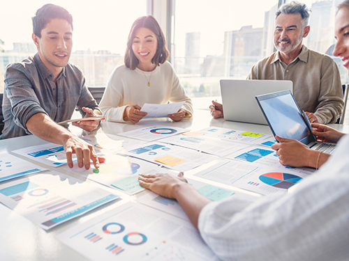 four people collaborating around a table and looking at charts and graphs
