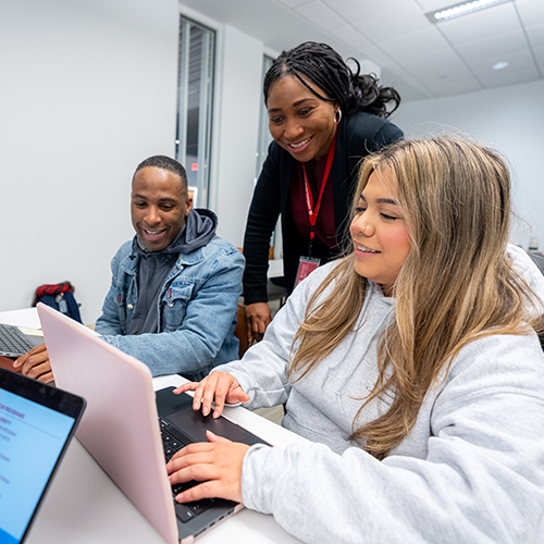 two college students looking at laptops with their professor