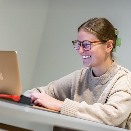 a woman wearing glasses smiling at a laptop