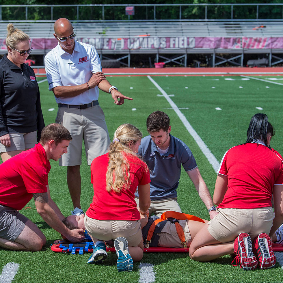 Students practicing taking care of an injured player at the Pitt Center and at the football field