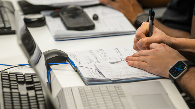Someone writing notes next to laptop