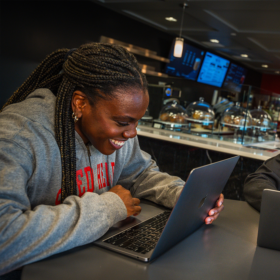 a person smiling while looking at a laptop in a coffee shop