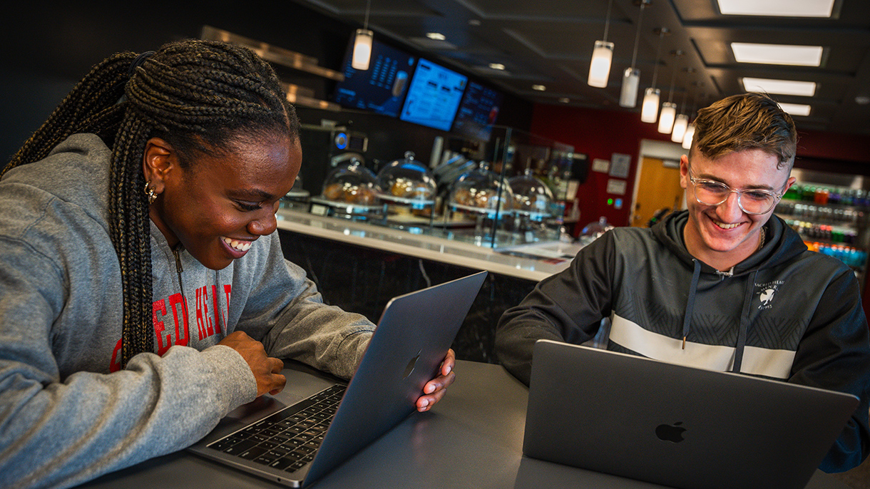a person smiling while looking at a laptop in a coffee shop