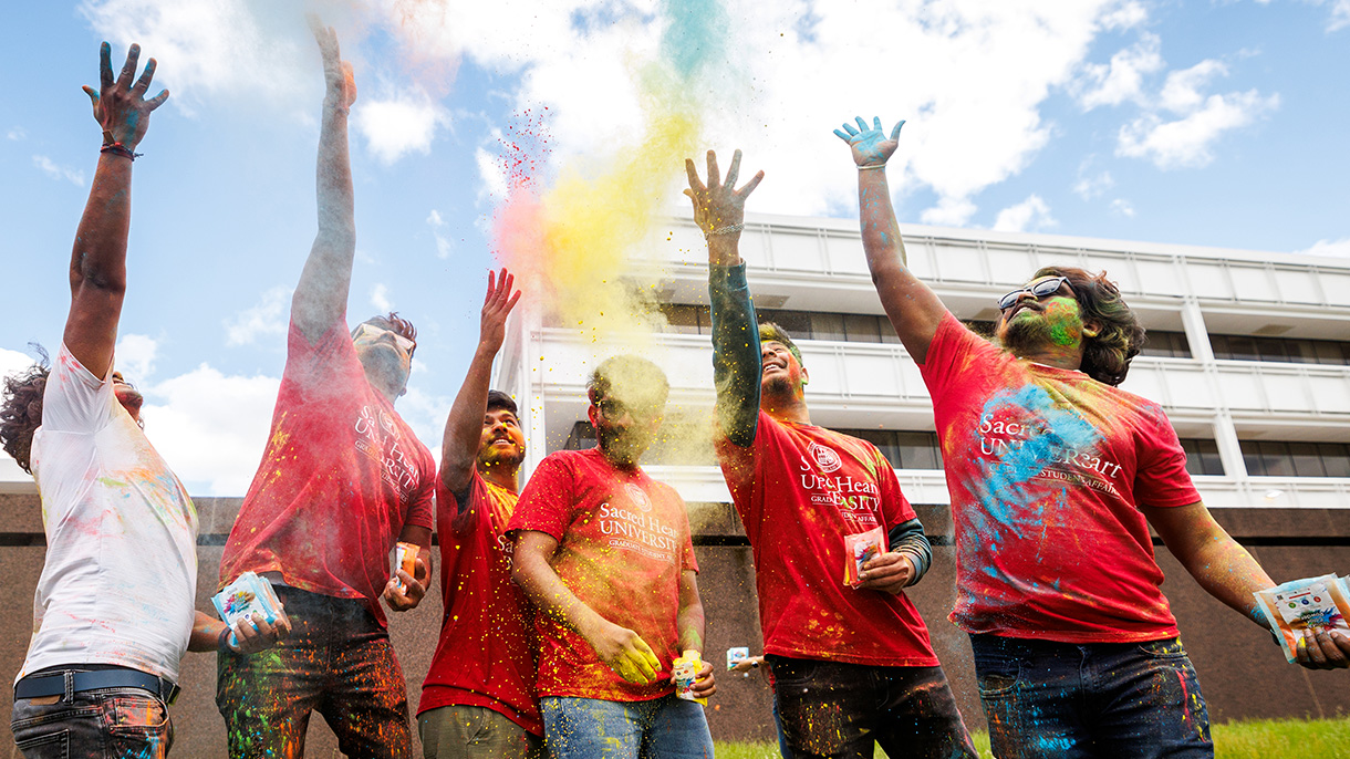 six people throw colorful gulal powder into the air as part of a Holi celebration