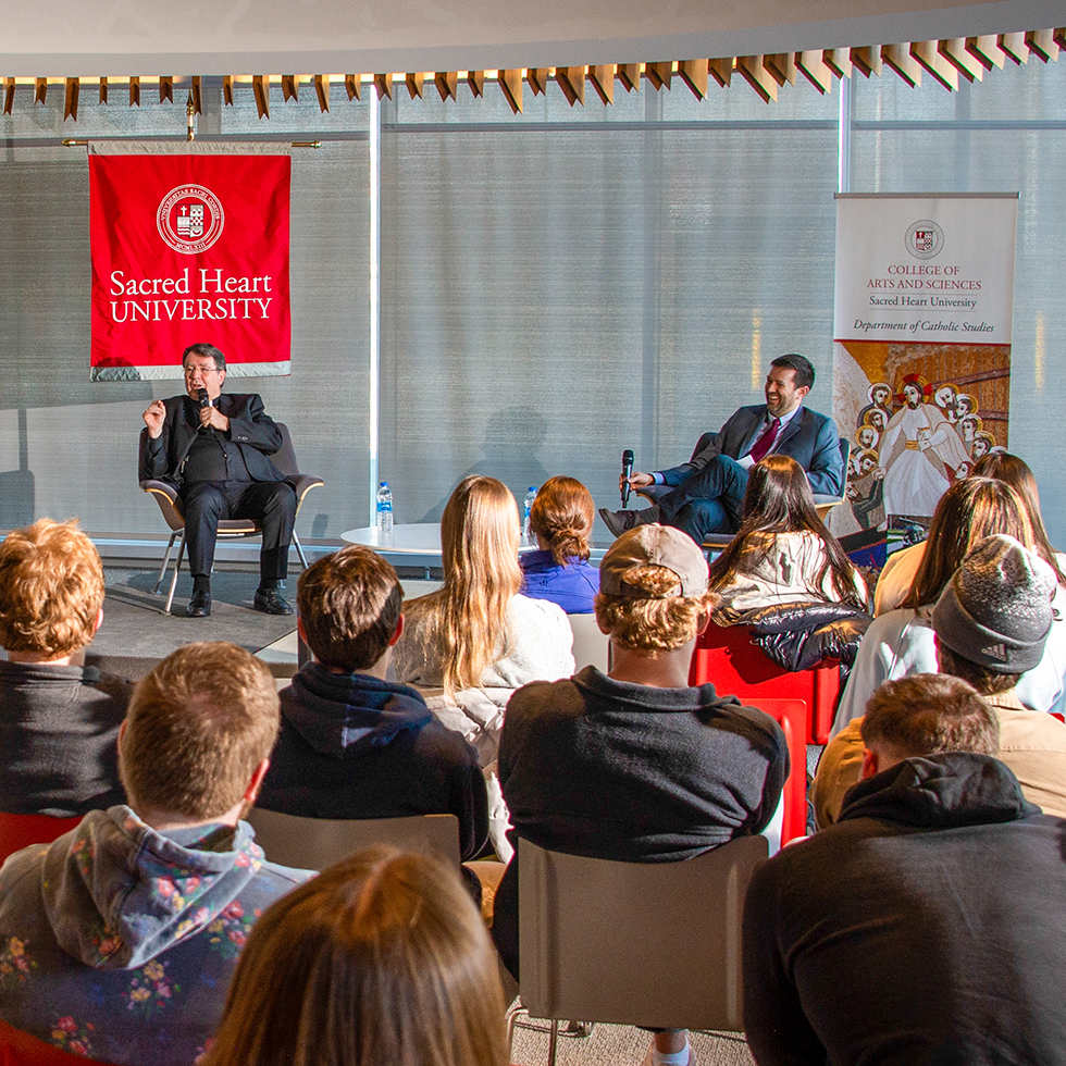 a priest speaker and moderator take questions from an audience