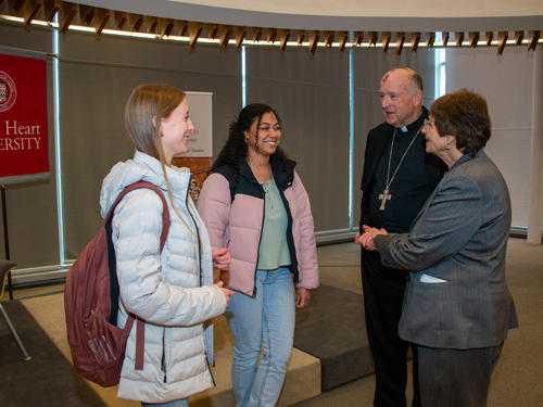 Two students talking to priest and Dr. Loris