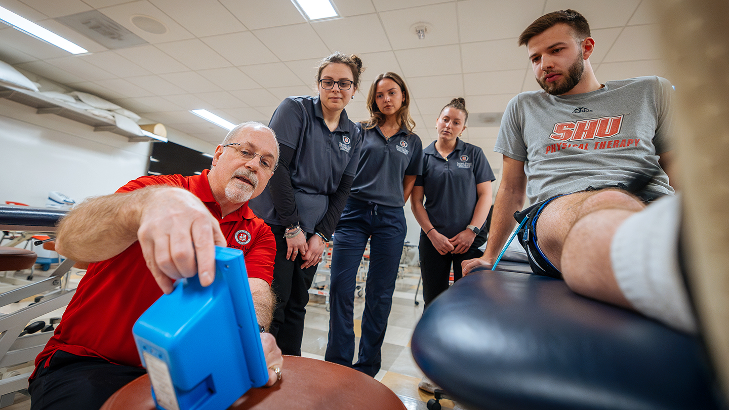 a professor showing four students the readout on a piece of physical therapy equipment