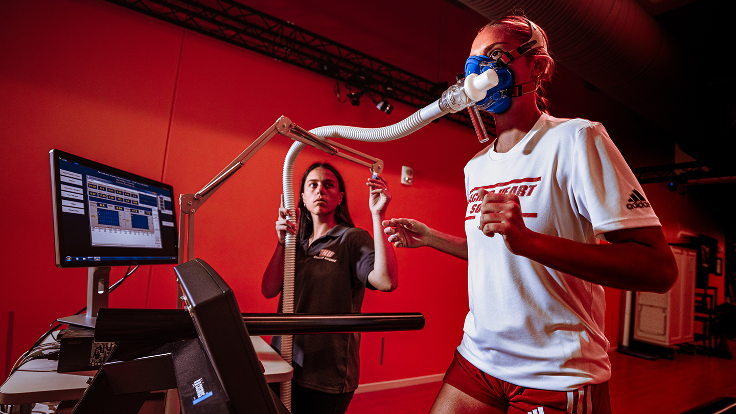 A person running on a treadmill with breathing analysis equipment and tubing on their face