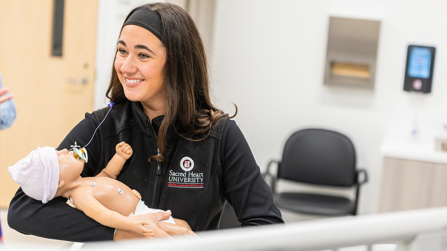 a student holding a speech language pathology pediatric manikin